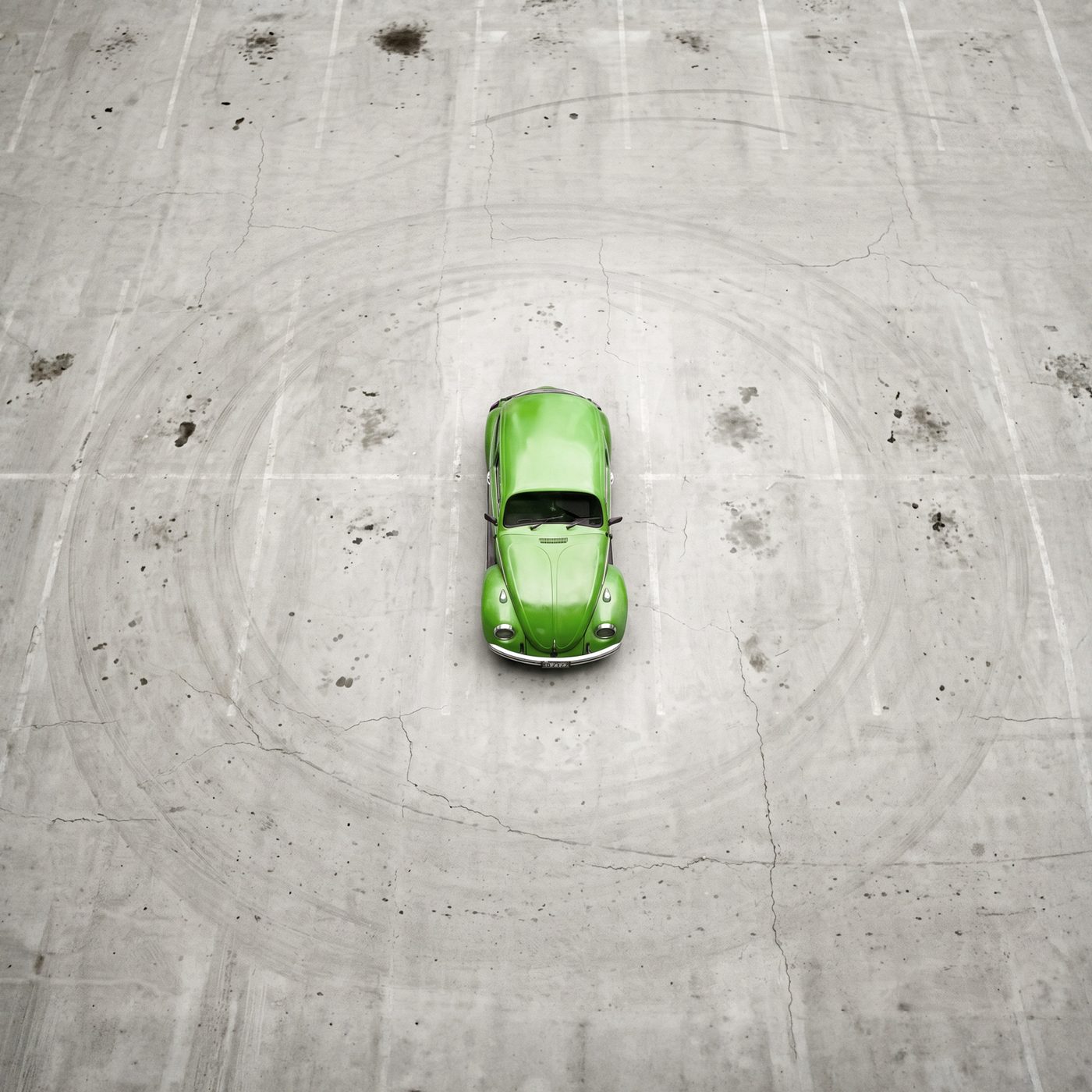 Un Maggiolino verde visto dall'alto, solo al centro di un parcheggio di cemento vuoto